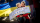 A child is holding a protest sign that says: “Putin, hands off Ukraine.” The child is sitting on their caregiver’s lap. Behind them is a Ukrainian flag.